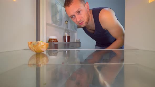 man looks into refrigerator, looks at onion and takes a bottle of alcohol.