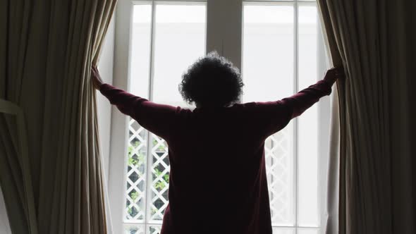 Rear view of senior african american woman opening curtains of the window at home