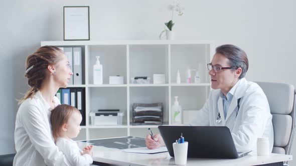 Male pediatrician is examining little baby. Doctor, mother and daughter in medical office.