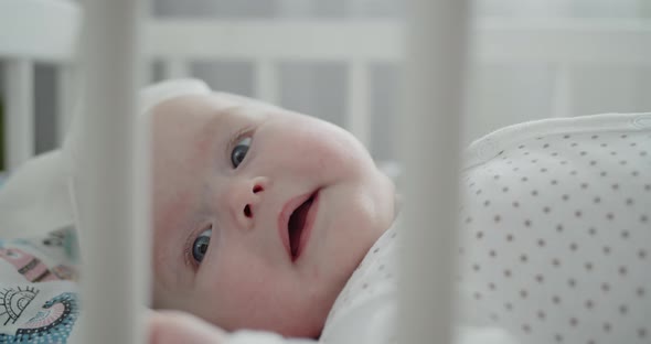 Closeup Portrait of a Cute Smiling Newborn Baby Lying in the Cradle Playing