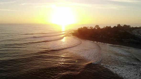 Aerial drone shot over Rincon Point surf break with ocean waves and surfers riding during sunset on