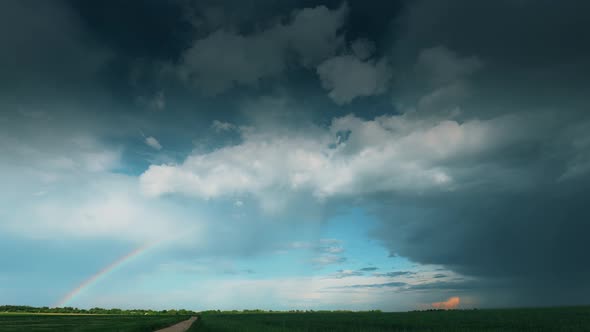 Dramatic Sky With Rain Clouds And Rainbow After Rain On Horizon Above Rural Landscape Country Road