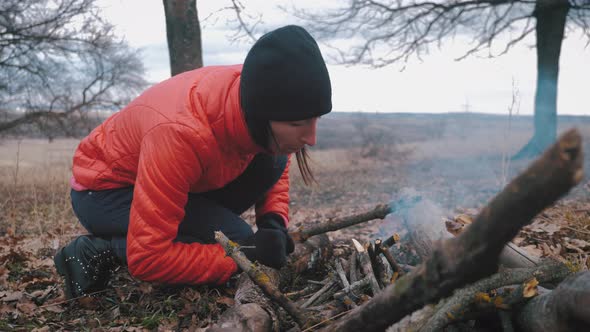 Girl Tourist Makes a Bonfire in the Autumn Forest During a Hike, Fire for Cooking and for Warmth