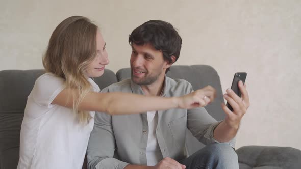 Smiling Young Couple Embracing While Looking at Smartphone