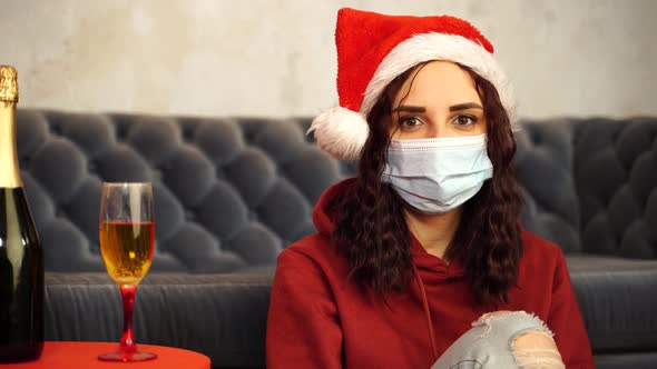 Young Woman in Medical Mask and Santa Claus Hat Sitting on Floor Near Sofa in Room