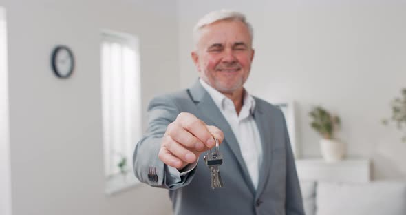 Shot of Apartment Keys Extended on Palm of Hand Toward Camera Grayhaired Mature Man Dressed in Suit