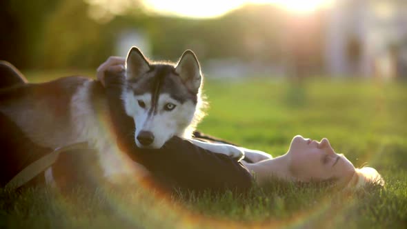 Beautiful Young Woman Playing with Funny Husky Dog Outdoors in Park at Sunset or Sunrise on Green