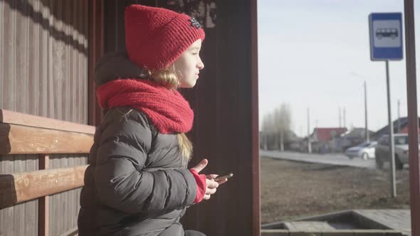  Little Girl Sitting on a Bench Waiting for Transport at the Bus Stop