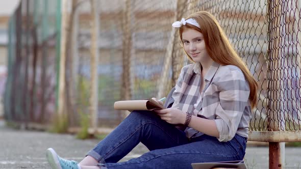 Teenage Girl Sitting Outdoors with Sketchbook and Smiling at Camera