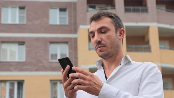 Focused Businessman in a White Shirt is Writing on the Phone Online