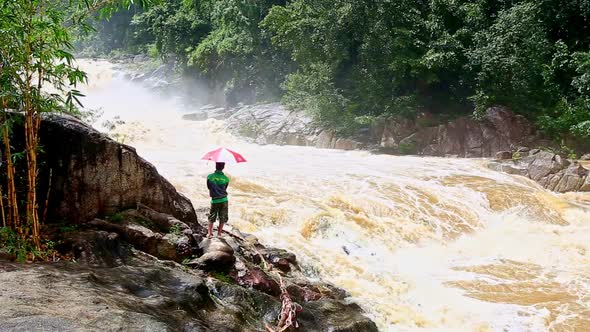 Man Stands on Rock Watches Stormy Powerful River in Mountains