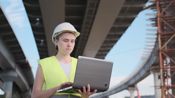 Young woman engineer supervises construction of road bridge under construction