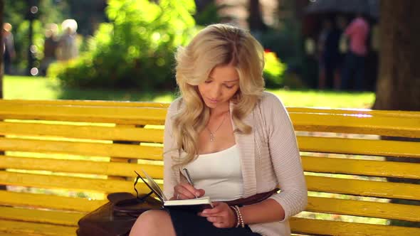 Young Adult Woman Writes Notes in Notebook Sitting Bench Park