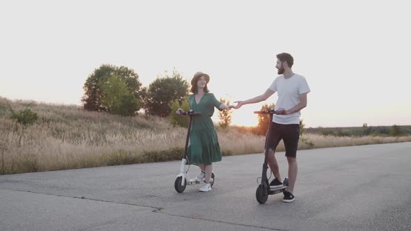 Couple in Love Holds Hands of Each Other During a Walk with Electric Scooters