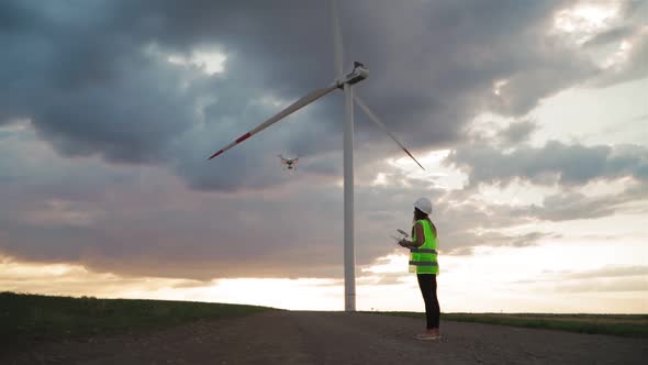 Professional woman Engineer in uniform hold remote controller for flying drone working wind turbine