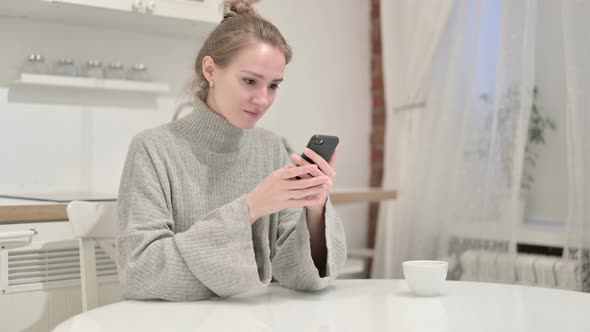 Cheerful Woman Celebrating Success on Smartphone at Home
