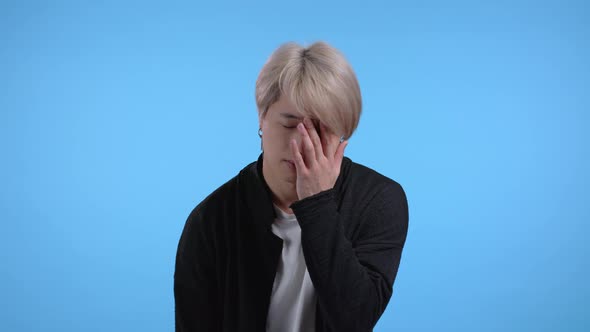 Bored Upset Asian Man Sighs on Blue Background