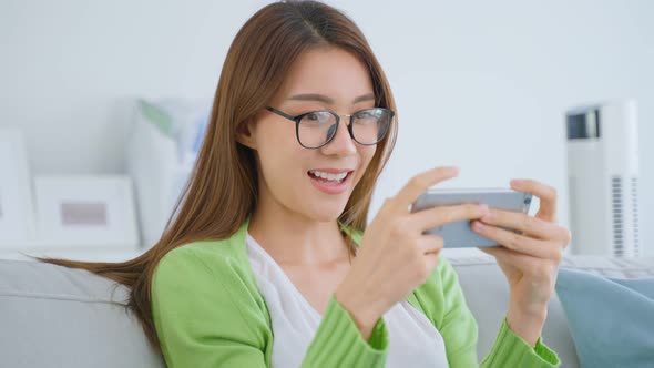 Asian e-sport gamer woman feel happy while play mobile game on cellphone in living room at home.