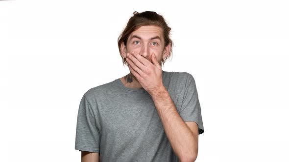 Portrait of Surprised Guy 20s with Tied Hair Covering Mouth with Hand in Joy and Excitement Isolated