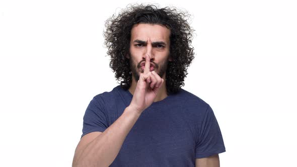 Portrait of Unshaved Caucasian Guy Posing with Strict Gaze and Asking Keep Quiet Putting Index