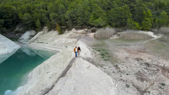 Couple Walks By Stony Lake Shore By Forest in Spain Aerial Pushout