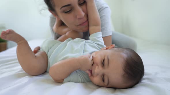 Happy mother playing with her baby lying together on bed