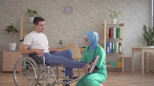 Muslim Doctor in Hijab Examines the Leg of a Disabled Person in a Wheelchair