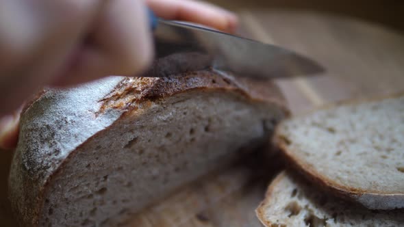 Close Up of Hands Slicing Loaf of Crusty Bread with Sharp Knife on a Wooden Board. 