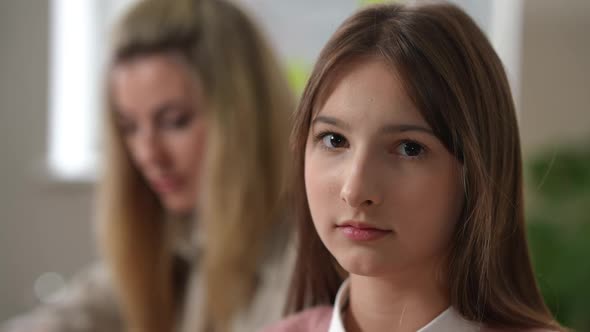 Headshot of Bored Disinterested Teen Girl Looking at Camera Rolling Eyes As Blurred Woman Explaining