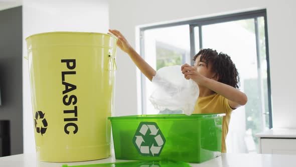 Happy biracial boy sorting plastic bottles and waste in kitchen