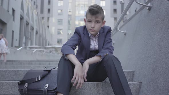 Pensive Cute Boy Wearing Business Suit Sitting on the Stairs on the Street