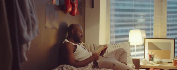 African American Man Reading Book on Bed at Home