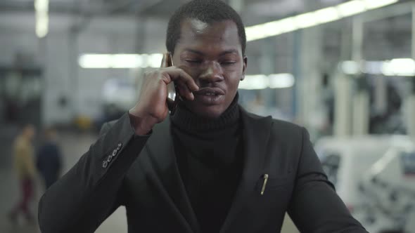 Portrait of Young Handsome African American Man Talking on Mobile Phone in Car Showroom
