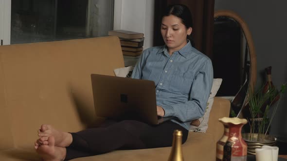 Asian Woman Works and Communicates with Friends or a Client Online, Sitting on the Couch
