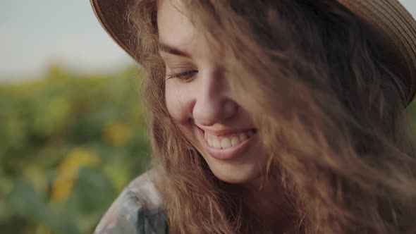 Portrait of Smiling Pretty Girl in Hat with Blowing Long Hair Among Sunflowers