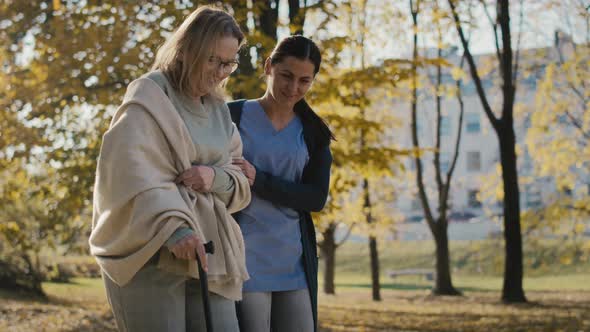 Young female nurse helping senior woman walking in park. Shot with RED helium camera in 8K