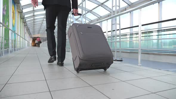 Feet of Successful Businessman Walking in Hall of Terminal and Pulling Suitcase on Wheels
