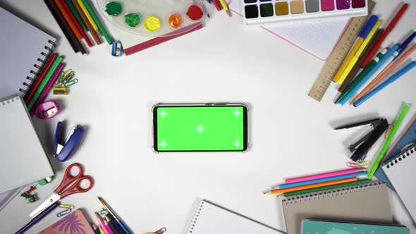 Man Put Smartphone with Chroma Key in Horizontal Orientation on the Table Full of School Supplies