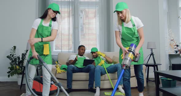 Mixed Race Men-Workers of Cleaning Service Sitting Together On Couch and Using Tablet PC