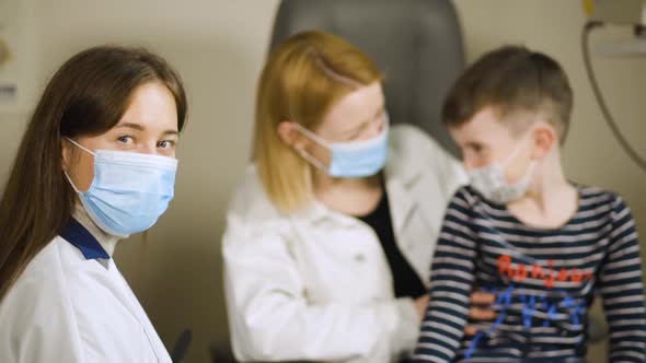 Female Eye Doctor in Medical Face Mask Patients Talking Behind. Hello in French on Sweater