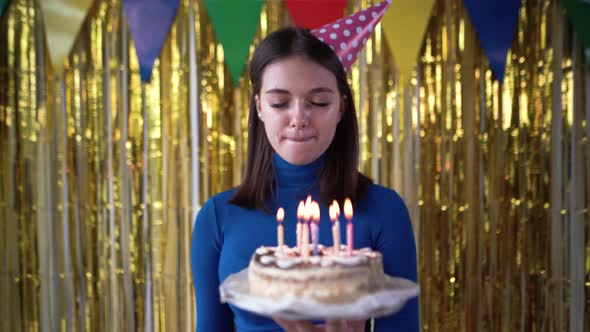 Caucasian Lady Millennial with a Cake in Her Hands at a Birthday Party Makes a Wish and Blows Out