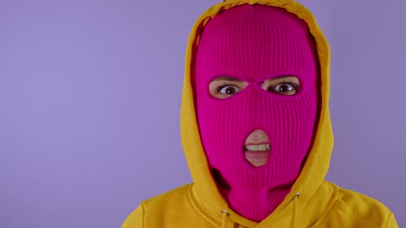 Close Up of Young Woman in Pink Balaclava and Yellow Hood Squints and Shows Her Teeth on Purple