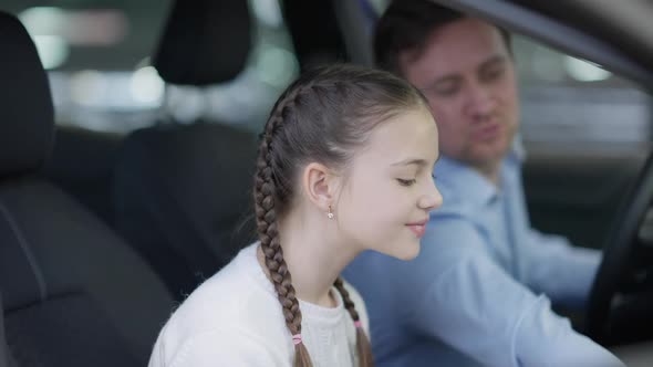 Closeup Side View of Excited Beautiful Caucasian Girl with Pigtails Sitting with Father in Car in