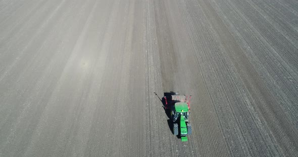 Aerial footage of farmer with tractor with seeder, sowing, seeding crops at agricultural field.