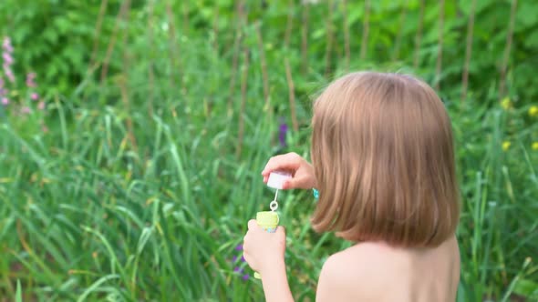 A Girl Inflates Soap Bubbles in a Meadow