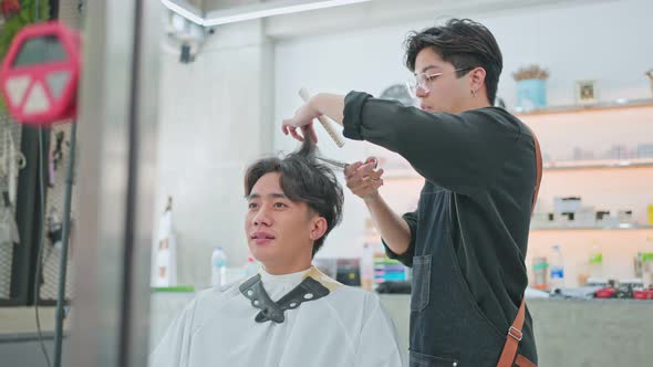 Asian professional male hairstylist combing and using scissors cutting young customer's hair.