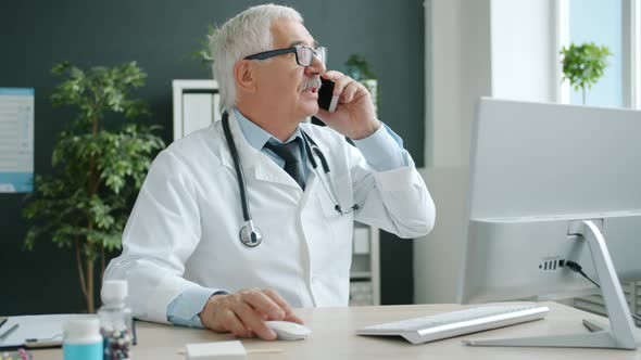 Medical Specialist Talking To Patient on Mobile Phone and Using Pc Working in Office