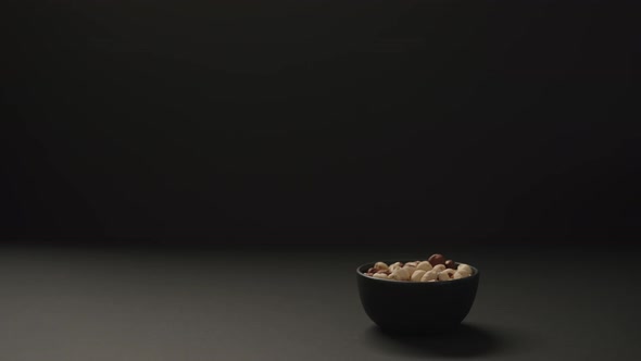 Slow Motion Man Put Roasted Hazelnuts Into Black Bowl on Black Paper Background