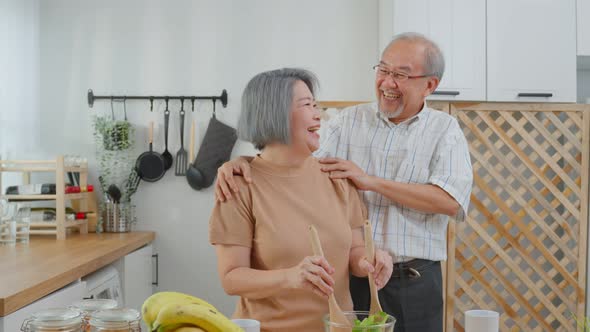 Asian senior elderly couple cooking salad together in kitchen at home.