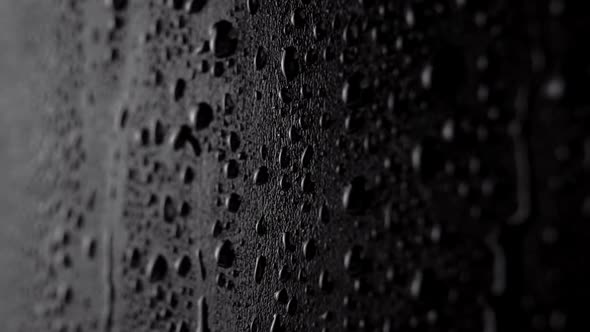 Spraying clean water on a textured vertical dark black surface in slow motion